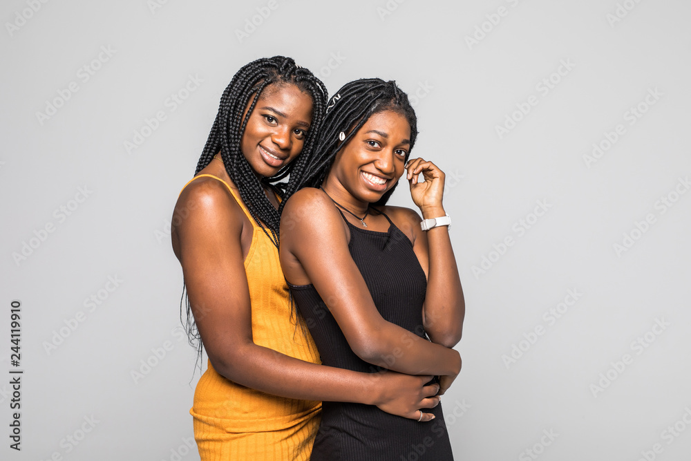 Portrait of two african women in dresses hugging isolated over gray background Portrait of two african women in dresses hugging isolated over gray background