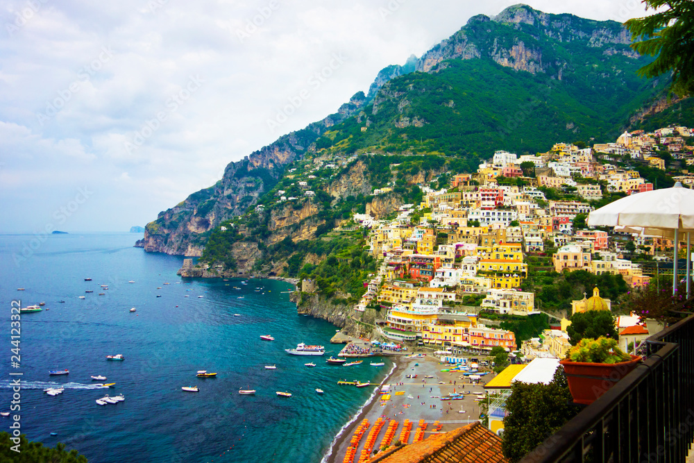 Colorful houses in Positano, Italy along blue water shore on a cloudy day