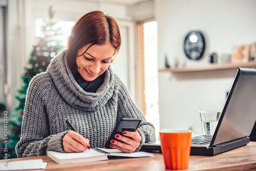 Woman holding smartphone and writing down notes in her notebook Woman holding smartphone and writing down notes in her notebook