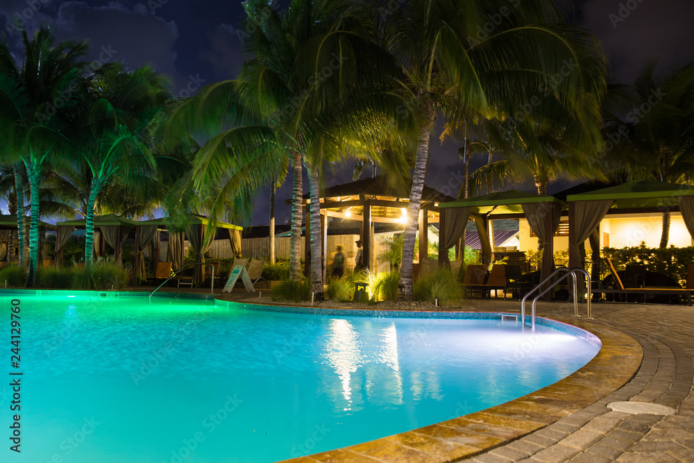 Beautiful resort hotel pool at night with lights and palm trees in tropical location
