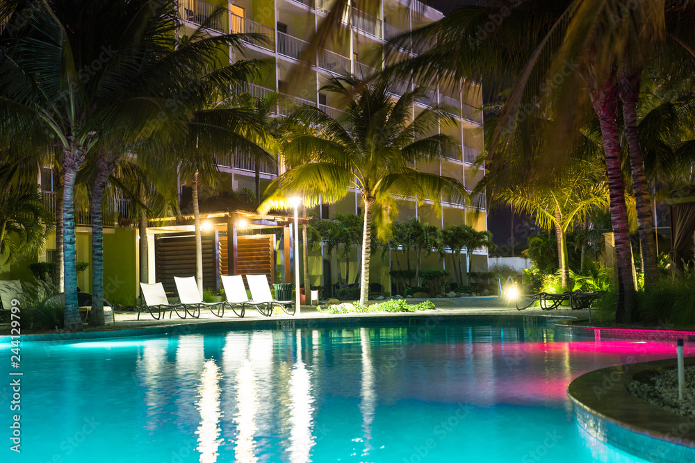 Beautiful resort hotel pool at night with lights and palm trees in tropical location