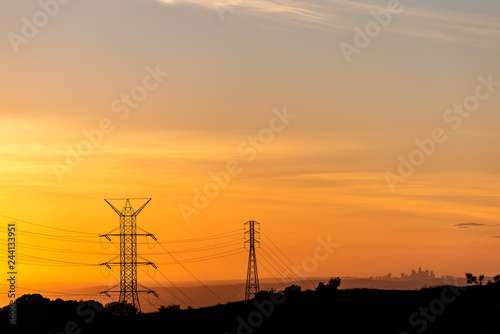 Silhoutte of Los Angeles skyline seen through power lines during a golden sunset.