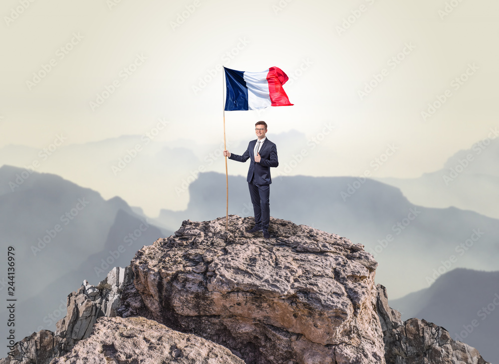 Obraz premium Successful businessman on the top of a mountain holding France victory flag 