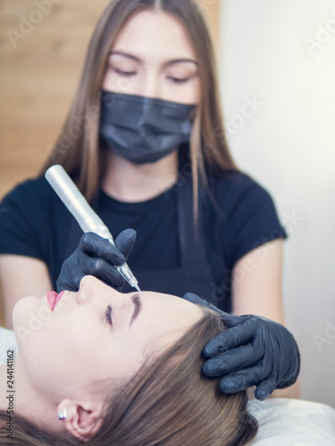 Master at work with the eyebrows makes microbleeding tattoo . Microblading eyebrows workflow in a beauty salon. Light brown girl do eyebrows needle.