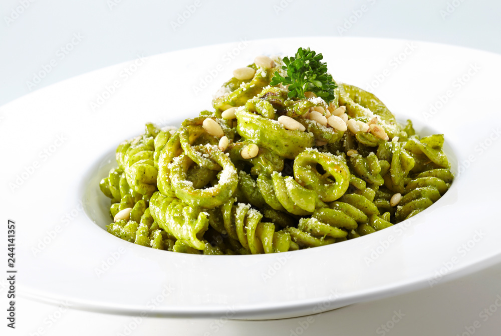 Delicious pine nuts with green sauce pasta over white background