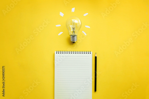 Flat lay of light bulb and empty memo pad and pencil on yellow background with texts. Conceptual brain storming still life. photo