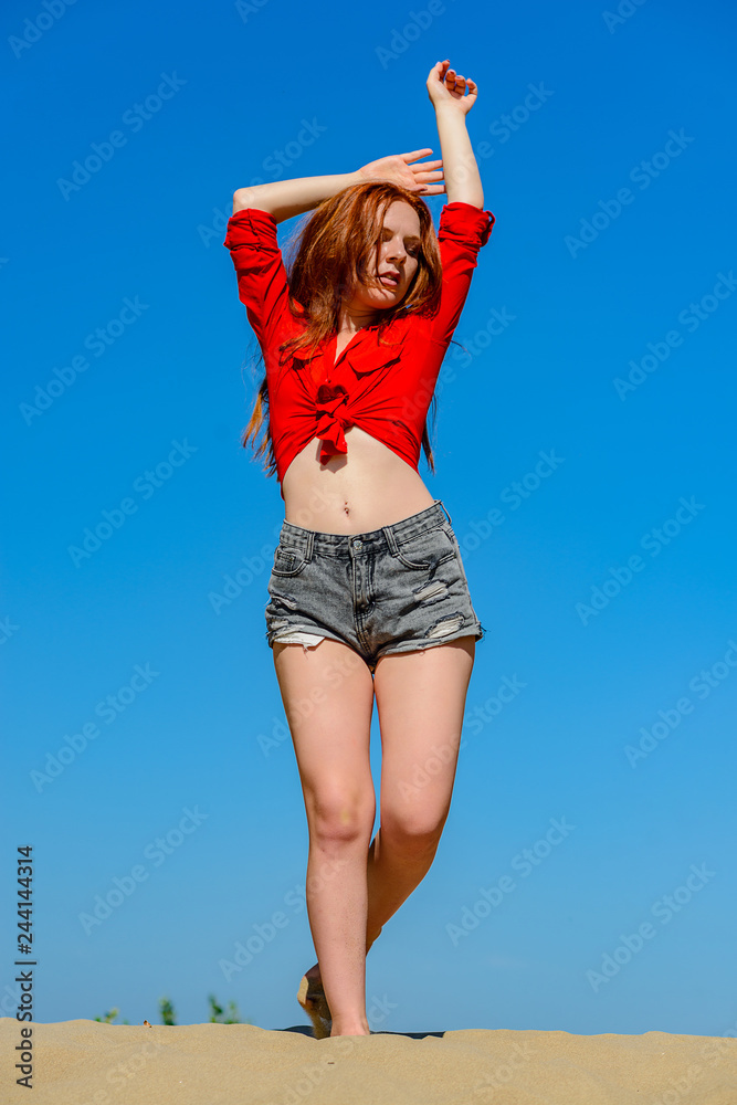 The portrait of the girl with red hair on sky background in sunshine day The portrait of the girl with red hair on sky background in sunshine day