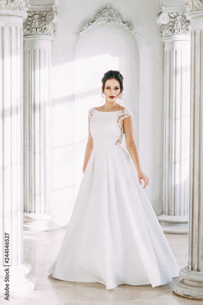 Fototapeta premium Beautiful girl in a wedding dress with a bouquet. Bride in a bright Sunny Studio.