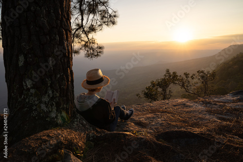 Woman sitting under pine tree reading and writing looking out at beautiful natural view photo