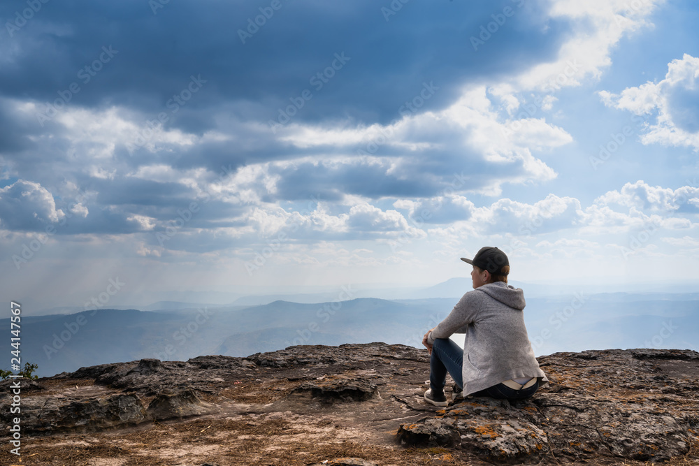 A person sitting  on rocky mountain looking out at scenic natural view and beautiful blue sky
