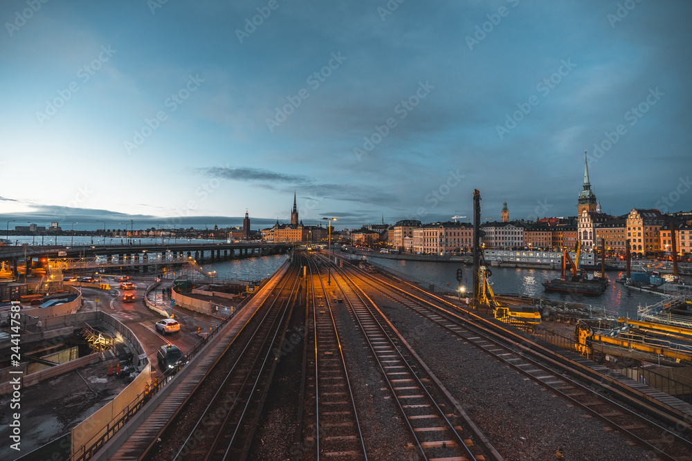 Evening cityscape with subway train crossing the bridge of Gamla Stan, Stockholm, Sweden. City hall and cathedral in background