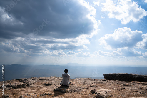 A person sitting on rocky mountain looking out at scenic natural view and beautiful blue sky