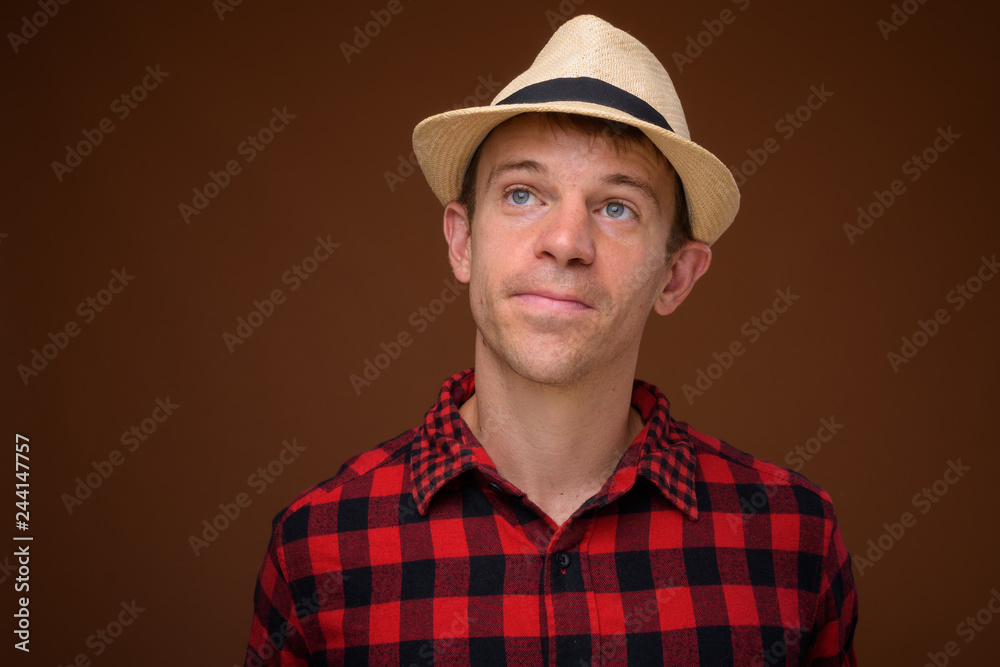 Tourist man wearing red checkered shirt and hat against brown ba Tourist man wearing red checkered shirt and hat against brown ba
