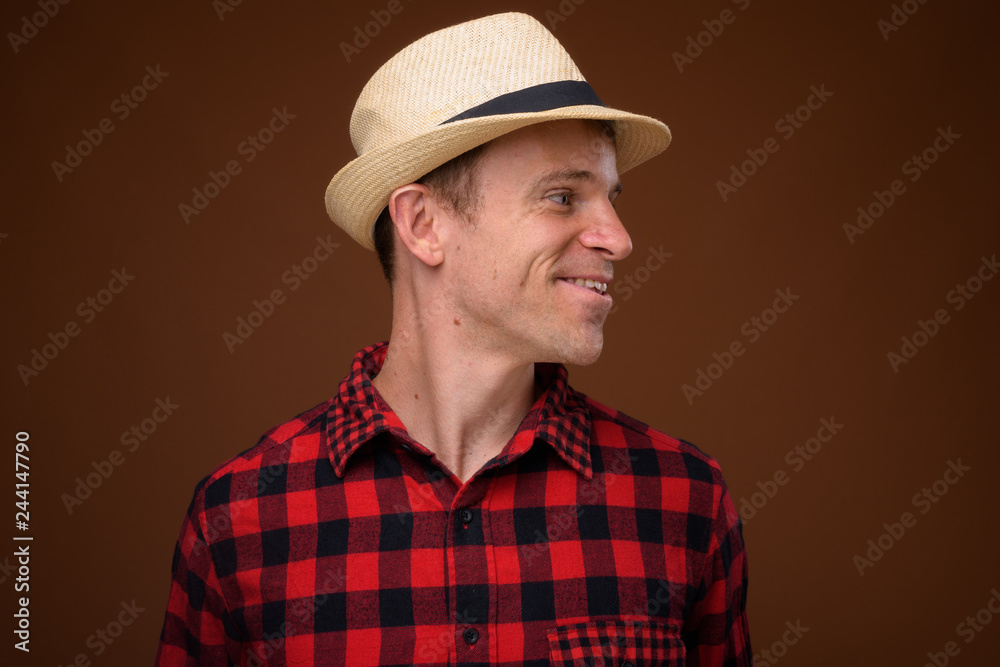 Tourist man wearing red checkered shirt and hat against brown ba Tourist man wearing red checkered shirt and hat against brown ba