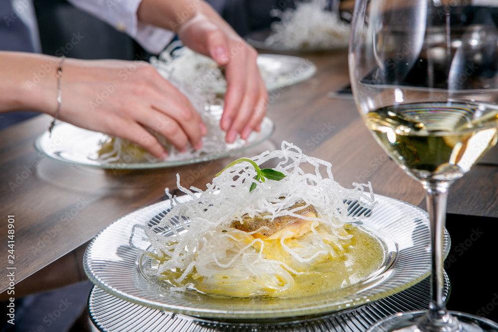 Chef decorates the halibut with mango sauce and rice noodles. Master class in the kitchen. The process of cooking. Step by step. Tutorial. Close-up Chef decorates the halibut with mango sauce and rice noodles. Master class in the kitchen. The process of cooking. Step by step. Tutorial. Close-up