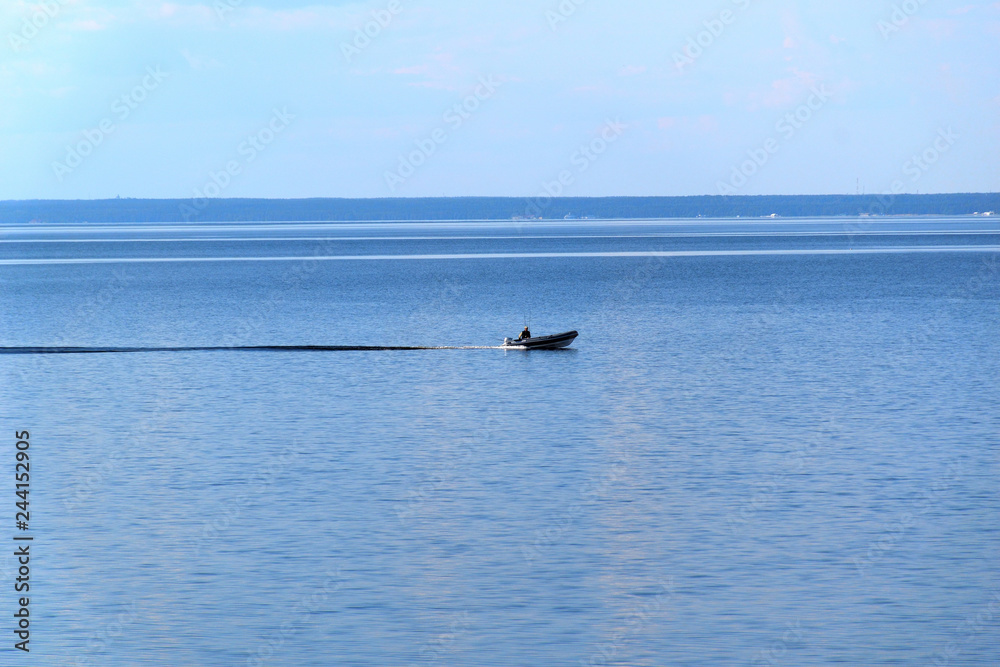 Fisherman on a motor boat sails on the water surface. Beautiful bright blue sky and water