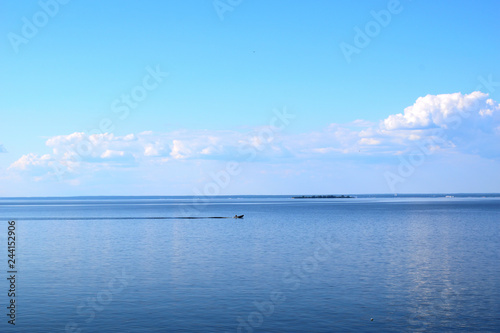 Fisherman on a motor boat sails on the water surface. Beautiful bright blue sky and water