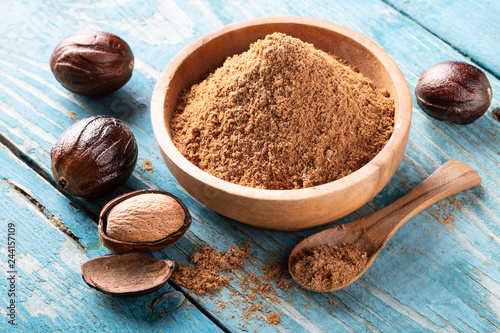 Whole inshell nut and nutmeg powder in a wooden bowl and spoon on old blue rustic background. photo