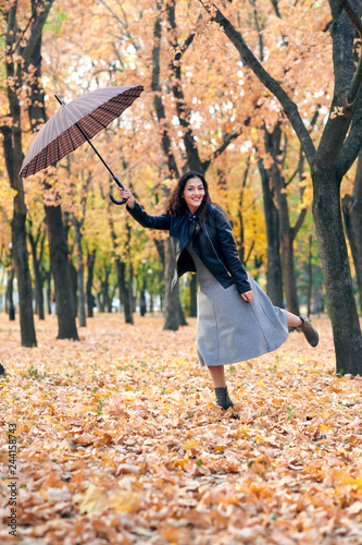 Woman with umbrella posing in autumn park. Bright yellow leaves and trees. She imitates the wind.