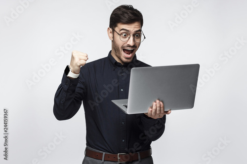 Happy excited  businessman holding laptop and raising his arm up to celebrate achievement, isolated on gray background photo