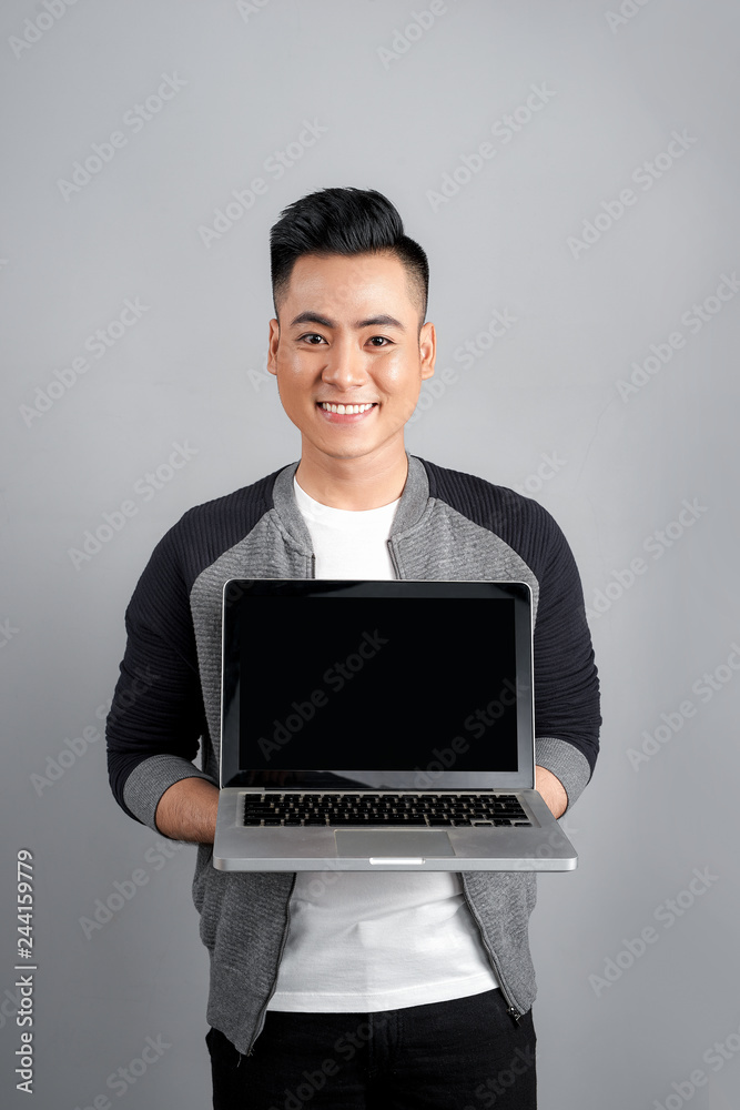 Portrait of a cheerful man showing blank laptop computer screen over gray background Portrait of a cheerful man showing blank laptop computer screen over gray background