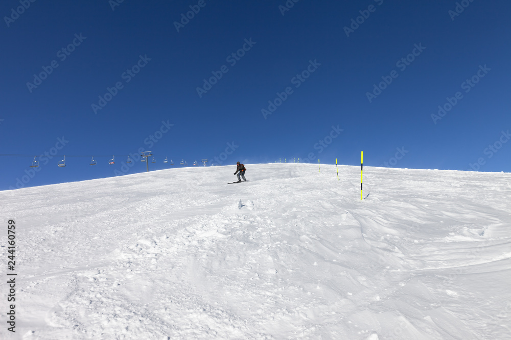 Skier downhill on snowy ski slope in sunny winter day