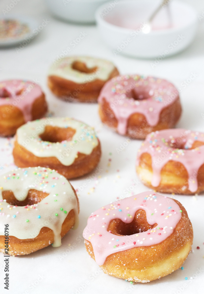Homemade donuts decorated with colored icing and colored sugar on a light background.