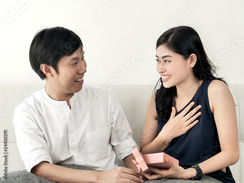Asian man surprising his girlfriend with pink gift box at home, valentine concept.