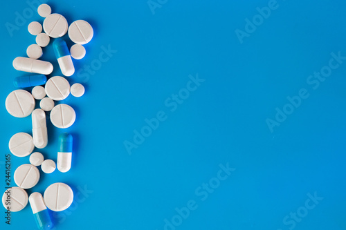 Obraz na plátne Scattered white pills on blue table