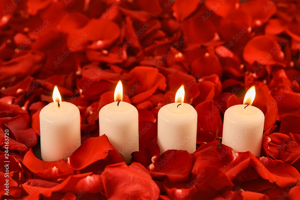four burning candles stand in red rose petals