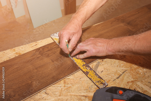 Worker is holding in hands a tape measuring. Power jigsaw for laminate flooring. Maintenance repair works renovation in the flat with scroll saw. Restoration of wooden parquet floor planks.