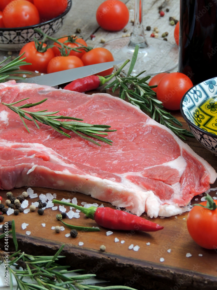 Raw meat steak, pepper, herbs, garlic and knife on wooden chopping board