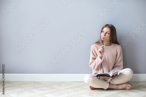 Young woman with notepad think hard sitting on a wooden floor.