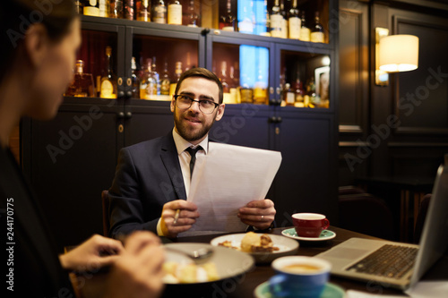 Confident businessman with papers discussing financial data with his colleague or partner at meeting in restaurant