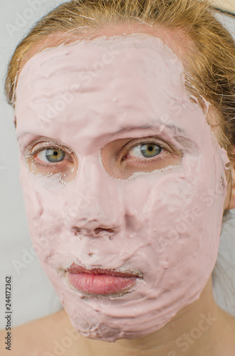 Good looking woman having a face mask on half of her face against plain background