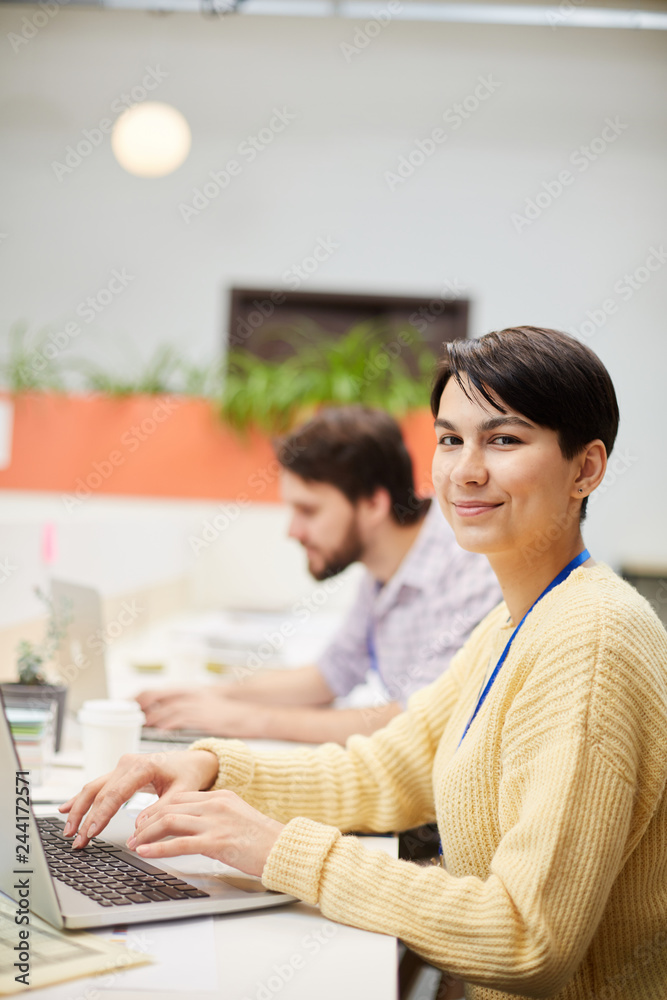 Happy young businesswoman in casualwear looking at you while browsing in the net by workplace