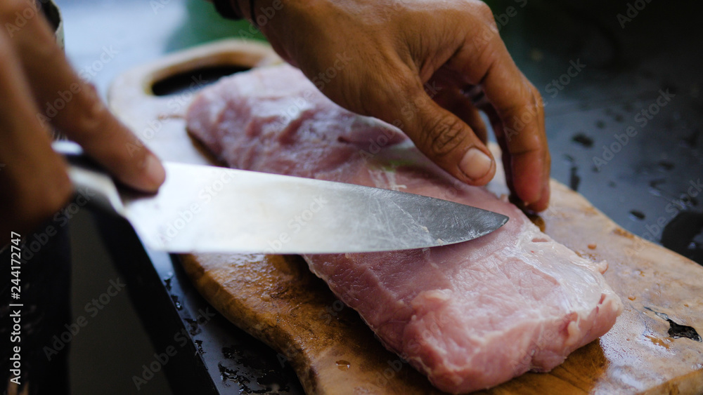 Chef cutting meat on wooden board. Butcher hands close up cutting meet.