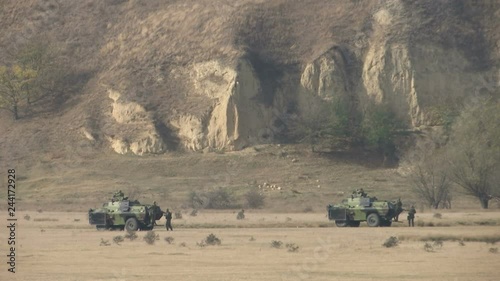 two military armored vehicles in the field with soldiers around them photo