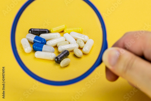 mixture of pills on a yellow background magnified by a magnifying glass