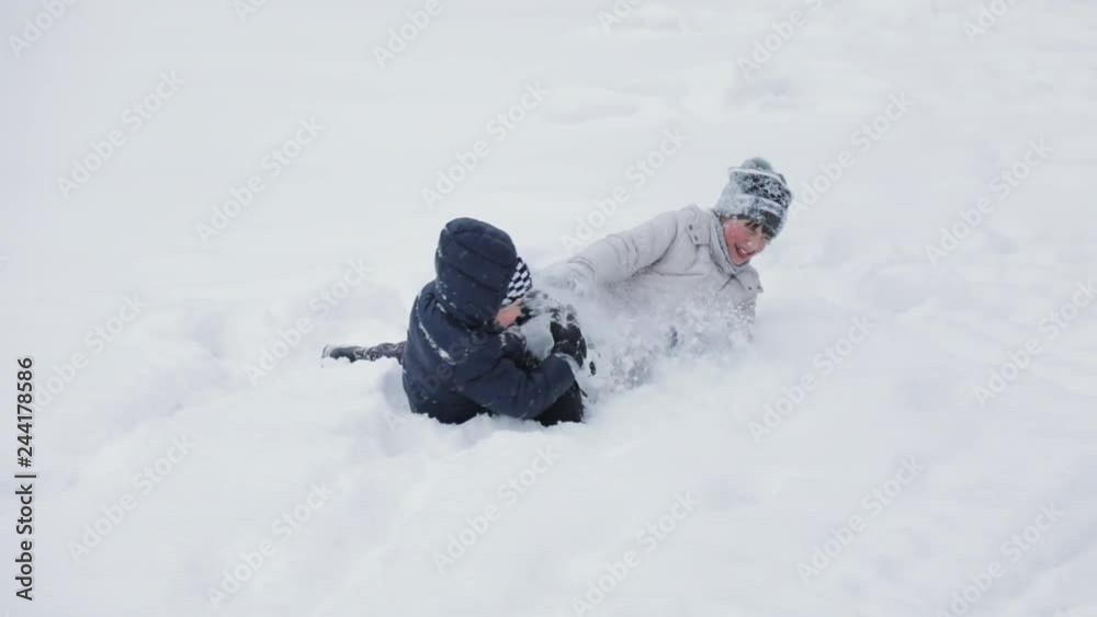 Slow motion view of two funny kids playing with snow while lying on the ground, carefree childhood concept Slow motion view of two funny kids playing with snow while lying on the ground, carefree childhood concept