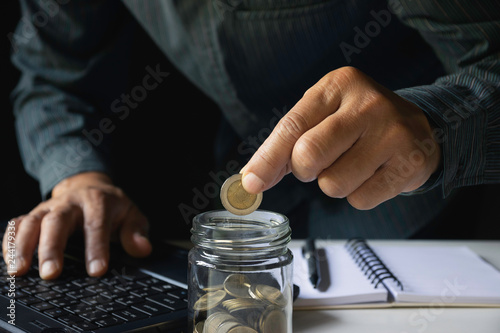 Business man putting coin in glass bottle saving bank and account for his money all in finance accounting concept.