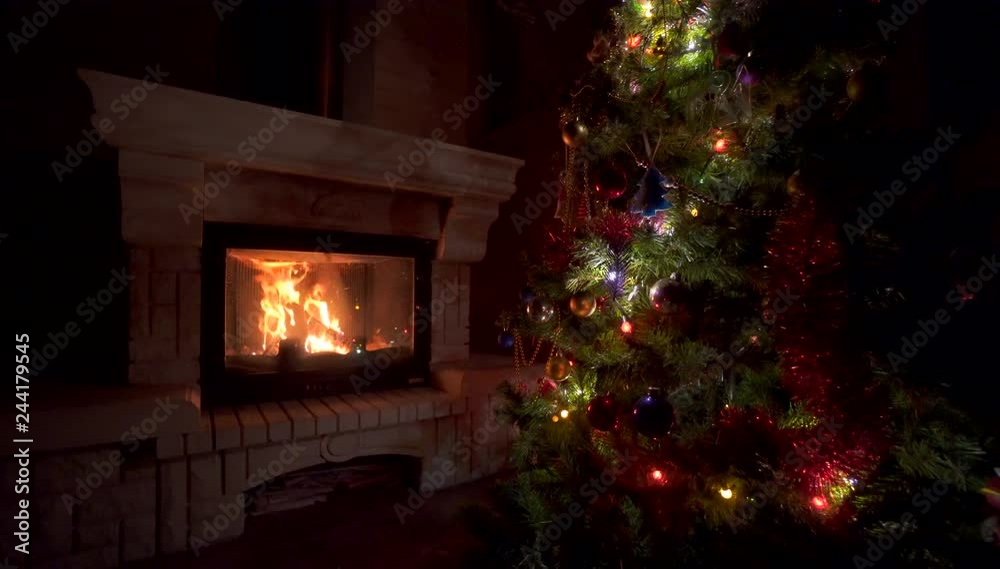 Amazing Christmas tree blinking colorful lights garland near fireplace with burning fire log. Beautiful cosiness holiday home interior enjoying winter vacation atmosphere Amazing Christmas tree blinking colorful lights garland near fireplace with burning fire log. Beautiful cosiness holiday home interior enjoying winter vacation atmosphere