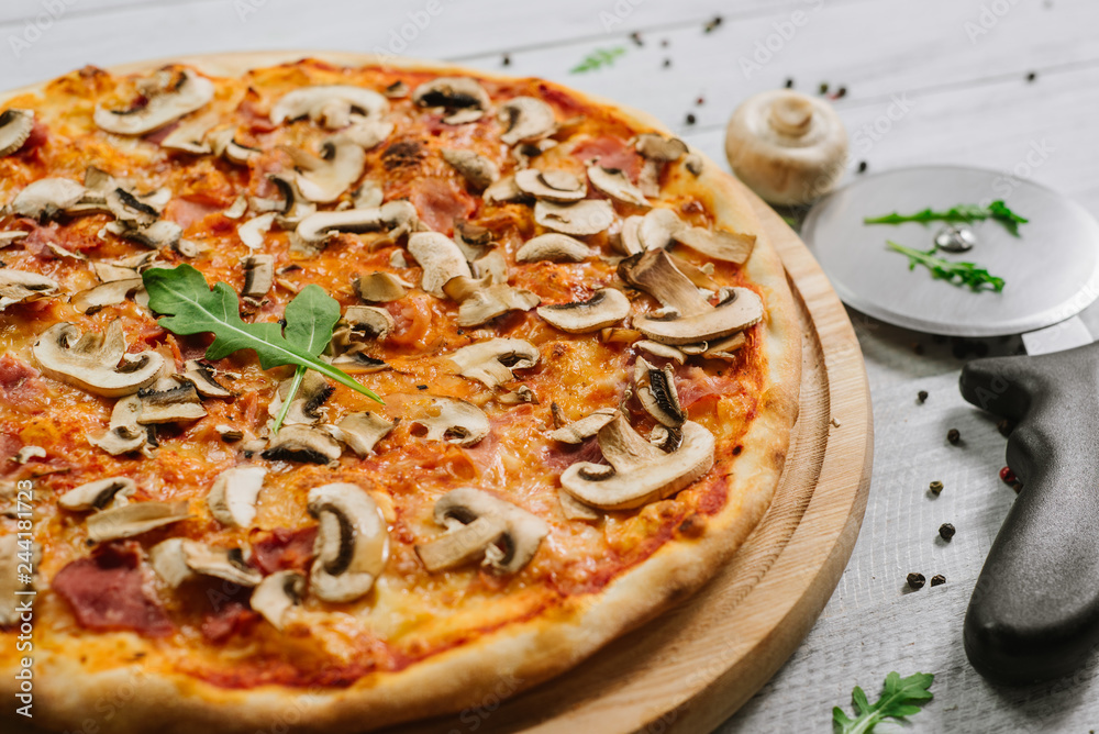 Tasty pizza Caprizzioza with tomato sauce, ham and champignons on the white wooden background