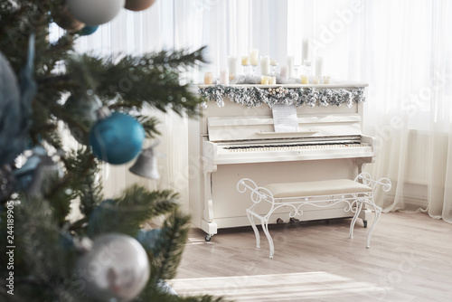 New Year decoration. Christmas tree near white piano at the window background