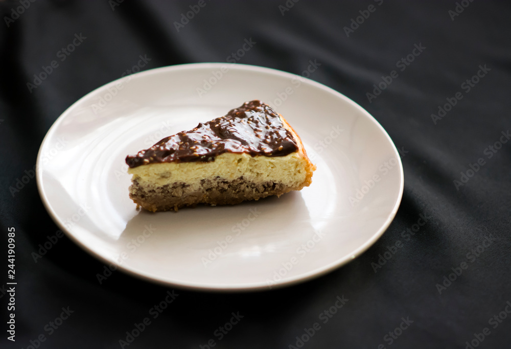 Piece of cheesecake with chocolate on a plate on black background