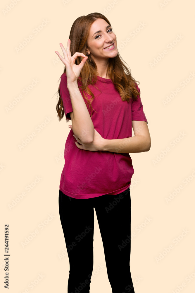 Young redhead girl showing an ok sign with fingers on isolated yellow background Young redhead girl showing an ok sign with fingers on isolated yellow background