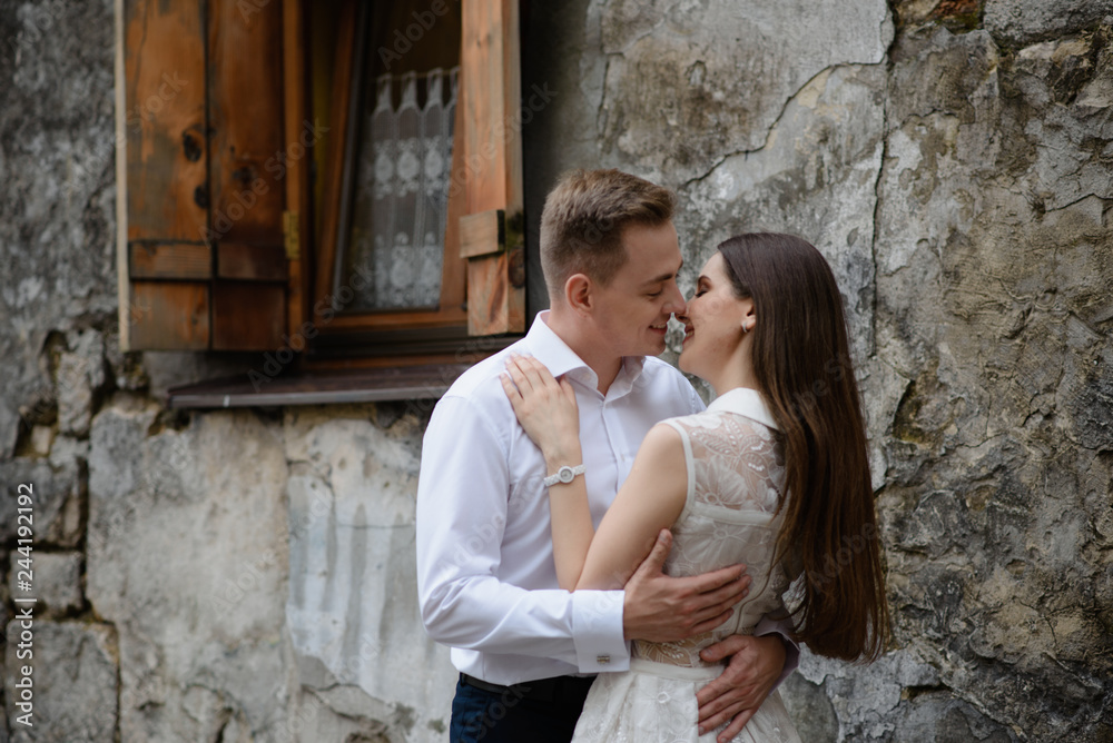 Couple in love is kissing and hugging over the grey urban wall in the morning city. Man and woman are having great time together. Ancient old european city street with stone walls. Couple in love is kissing and hugging over the grey urban wall in the morning city. Man and woman are having great time together. Ancient old european city street with stone walls.