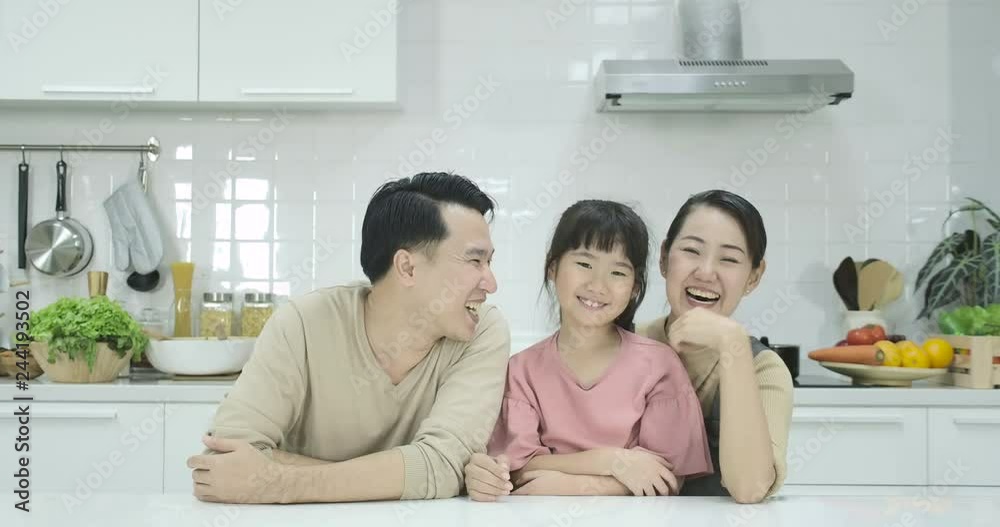 Happy asian family of mother, father and daughter sitting in the kitchen and smiling in front of the camera. Portrait shot. Indoors Happy asian family of mother, father and daughter sitting in the kitchen and smiling in front of the camera. Portrait shot. Indoors