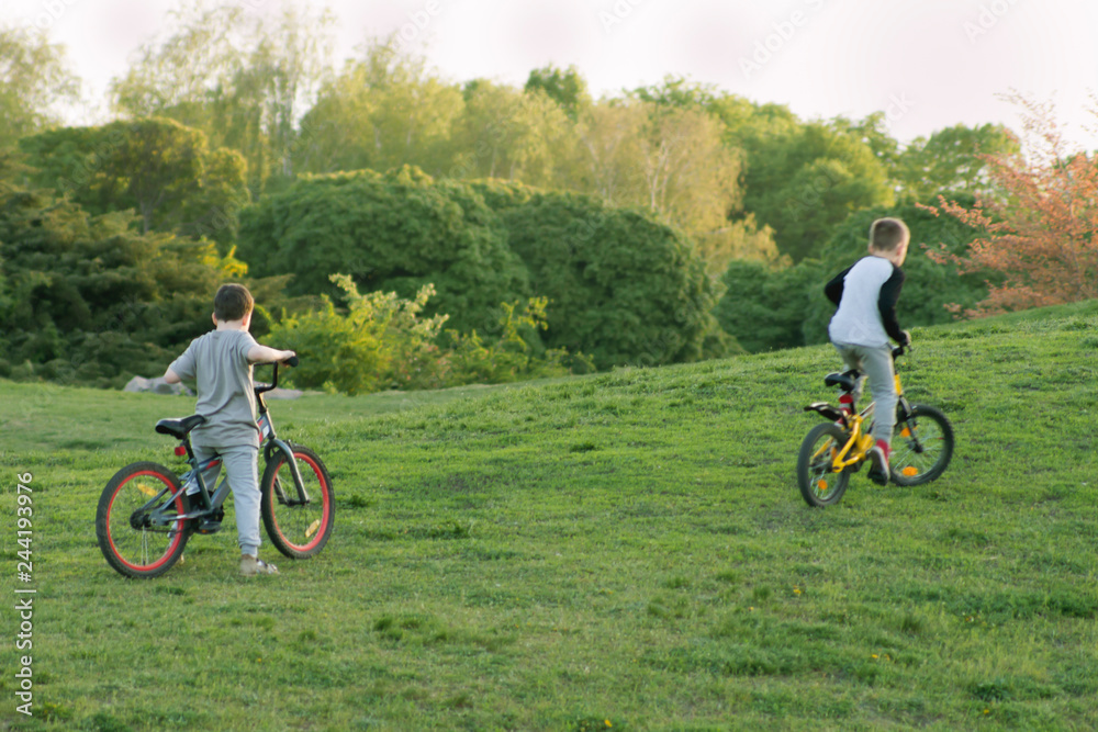 Two blured boys ridding bicycles on a beautiful green nature landscape and sunlight background Two blured boys ridding bicycles on a beautiful green nature landscape and sunlight background