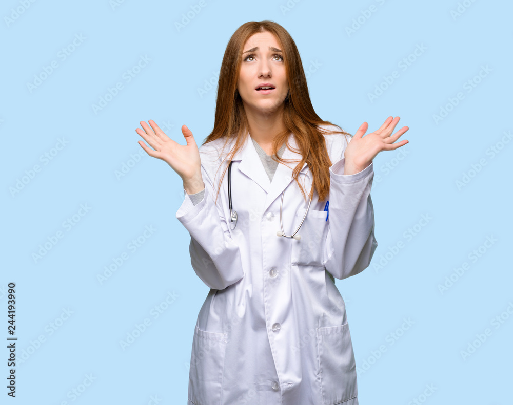 Redhead doctor woman frustrated by a bad situation on isolated blue background Redhead doctor woman frustrated by a bad situation on isolated blue background